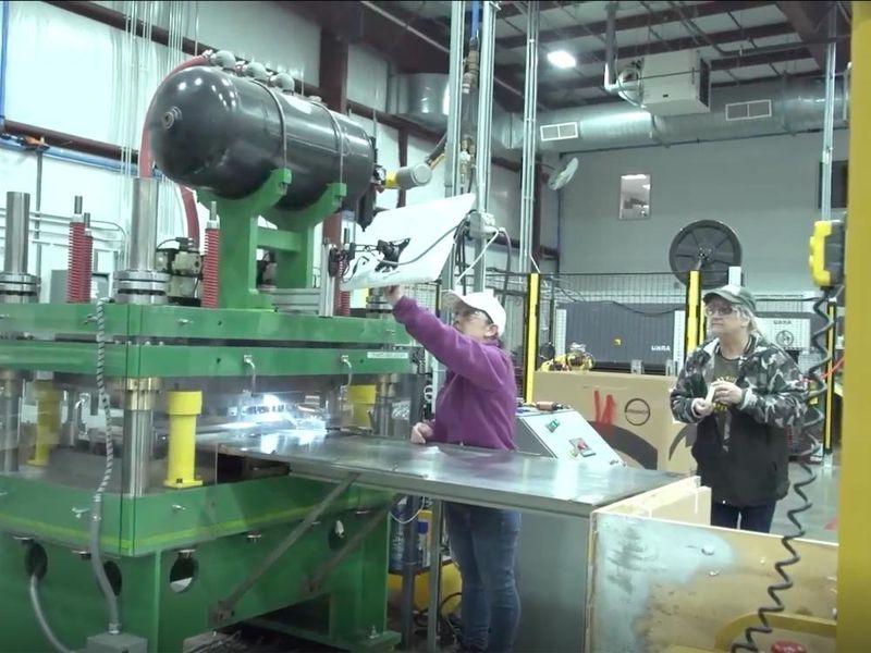 Two people in baseball caps and safety glasses work in a manufacturing plant 